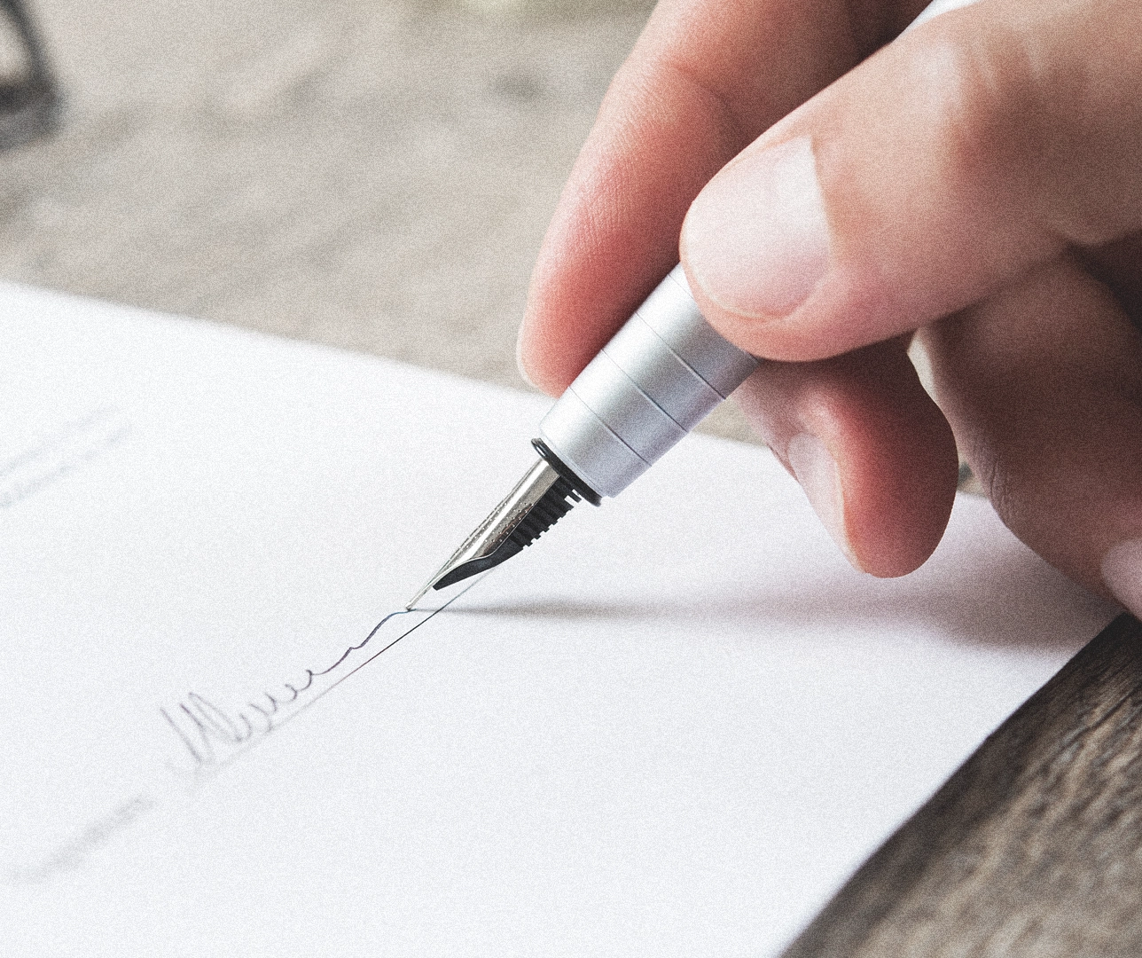 Primer plano de una pluma sujetada por una persona firmando un contrato.