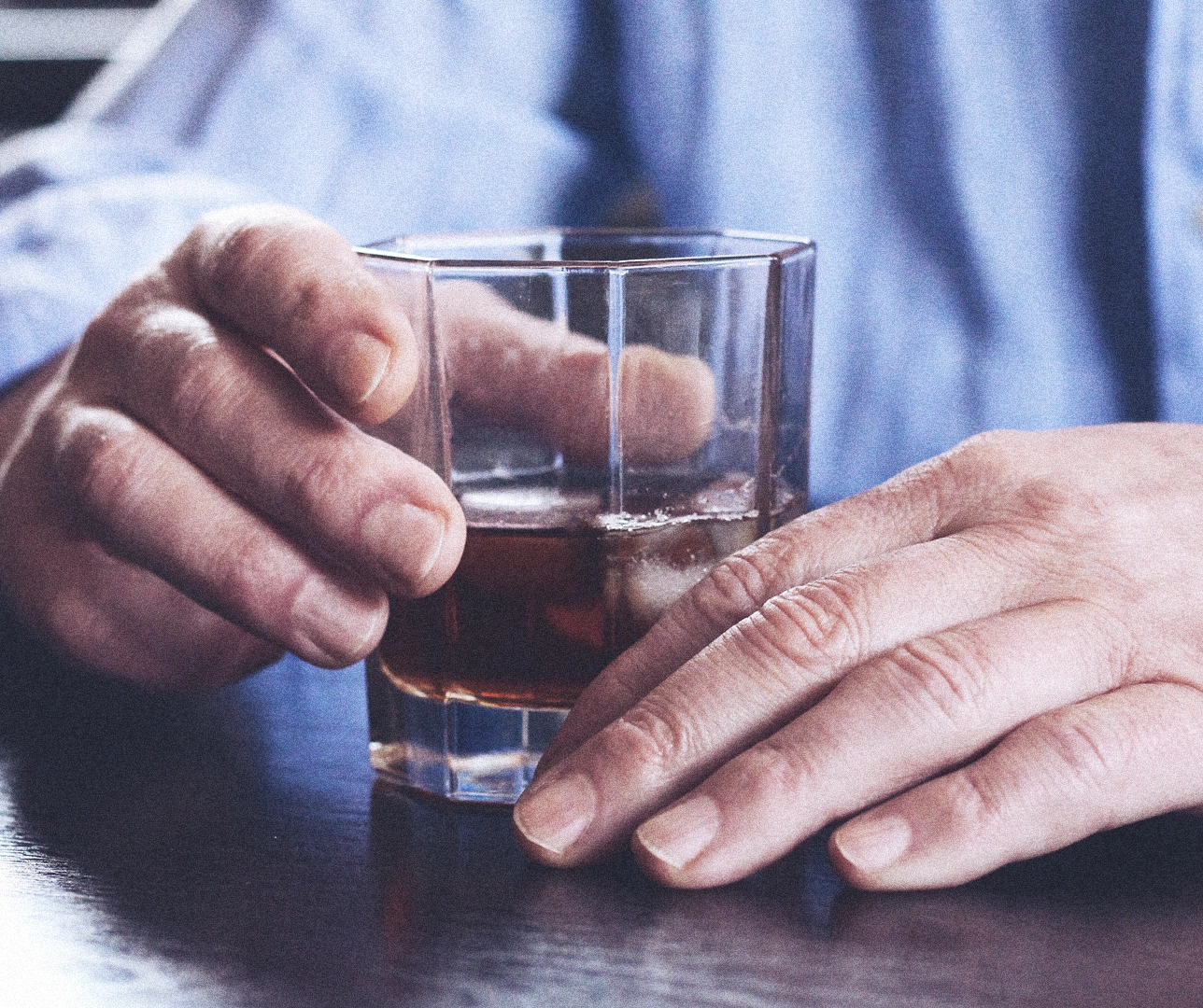 Imagen de un vaso de una bebida alcohólica sujetada por las manos de una persona.