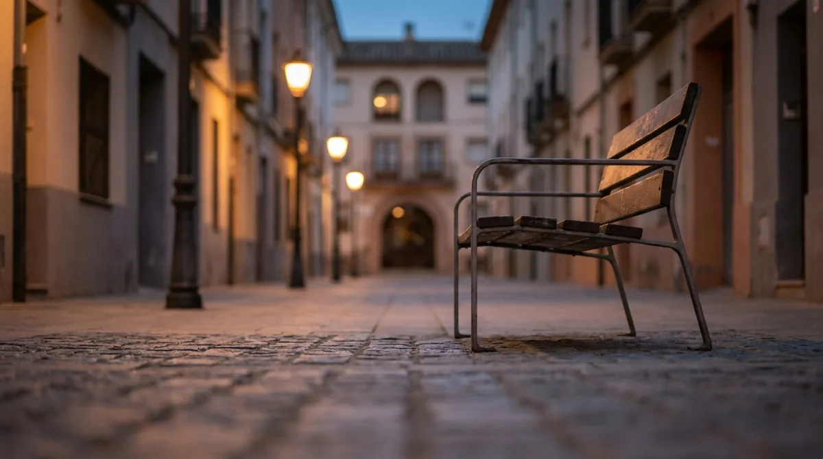 Calle vacía al anochecer con un banco en primer plano y un portal al fondo, imagen de la distancia que impone una orden de alejamiento